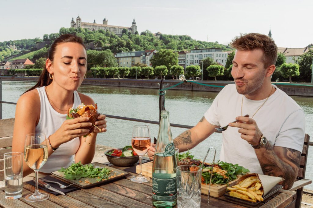 Ein Mann und eine Frau essen im Freien Burger und Steak mit Blick auf die Festung Marienberg Würzburg