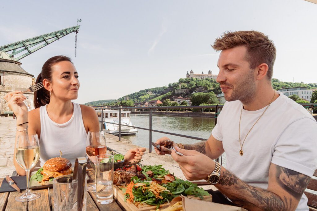 Ein Mann und eine Frau essen im Freien Burger und Steak mit Blick auf die Festung Marienberg Würzburg